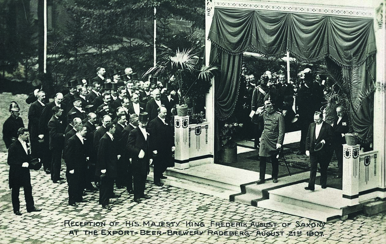 Numerous men stand up and to the left of a stage.
