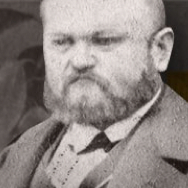 A corpulent man with a beard wears a suit and looks serious.