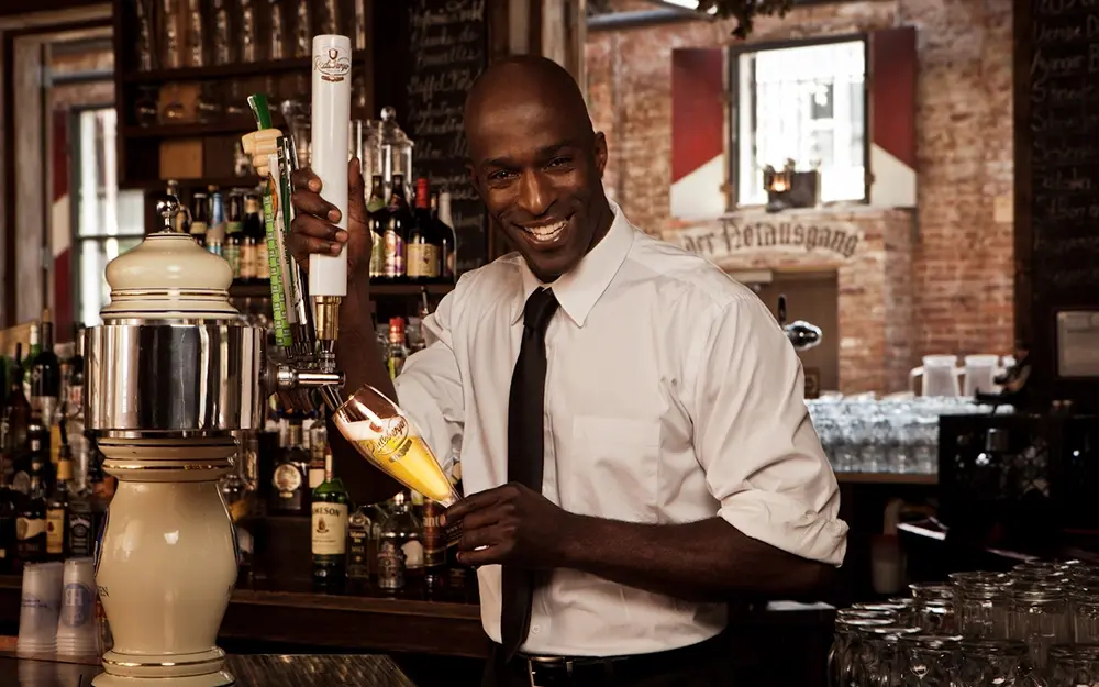 Bartender pouring beer from a tap into a branded radeberger glass behind a bar counter.