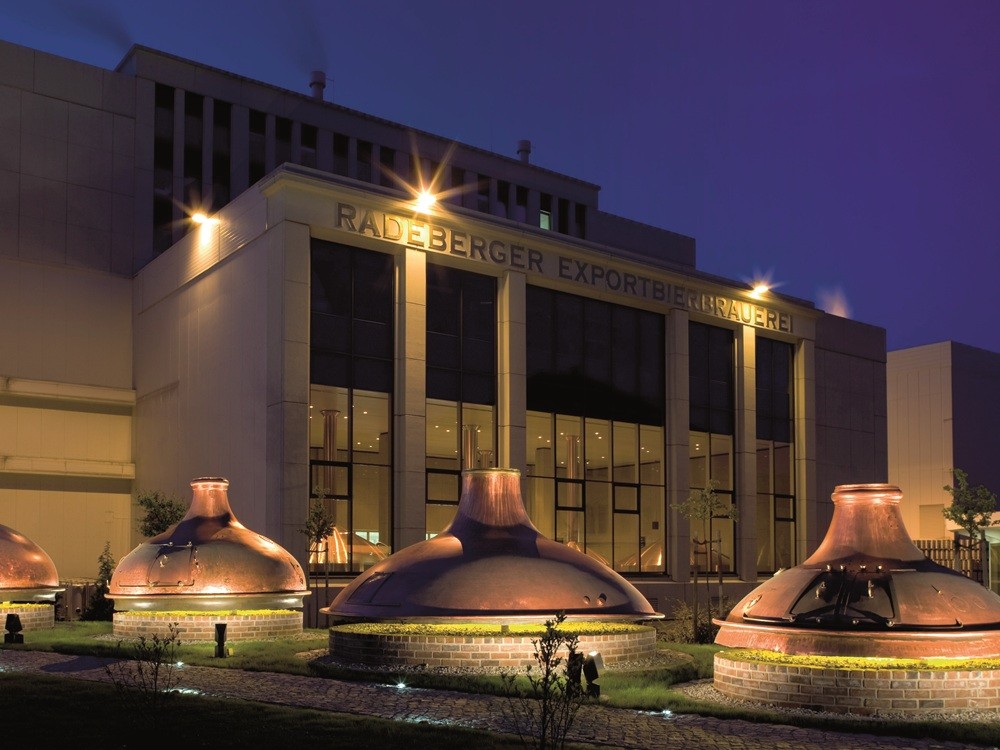 Three large copper kettles stand illuminated in front of a modern building at night.