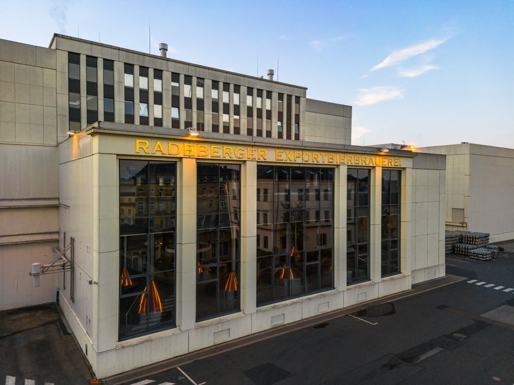 Large industrial building at dusk with interior lighting on and clear skies.