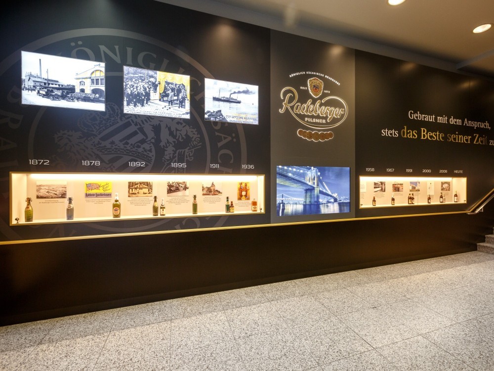 An exhibition wall with historical photos and labels in chronological order from 1872 to the present day.
