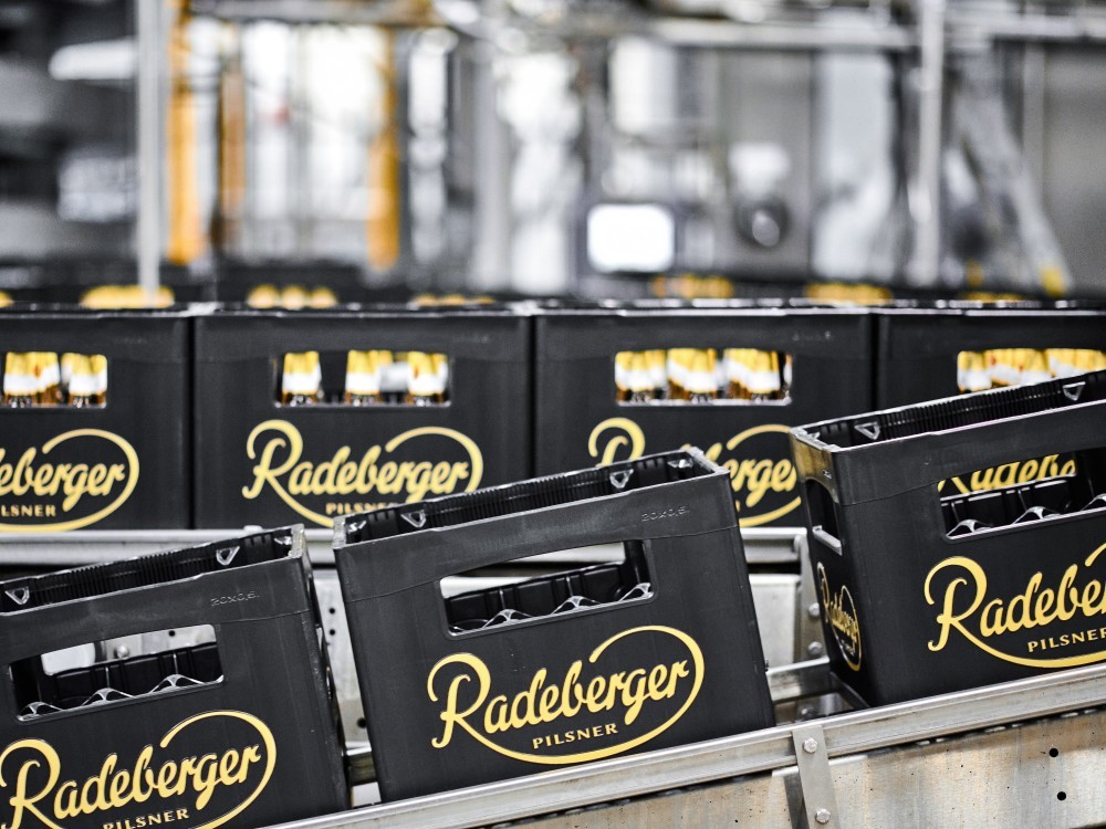 Rows of beer crates on a conveyor belt in a brewery are ready for distribution. Each crate is filled with bottles.