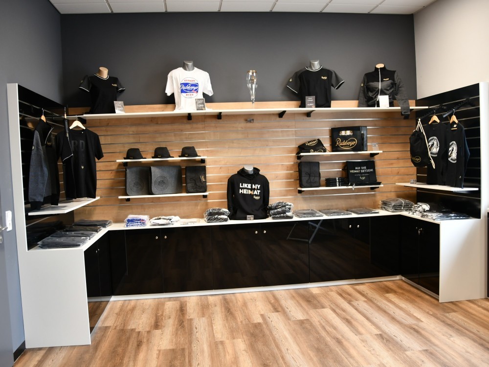 T-shirts, hats, and bags are on display in a clothing store. Wooden floors and dark walls create a modern atmosphere.