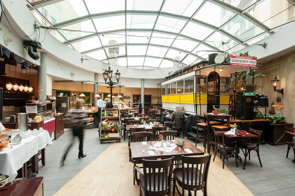 Restaurant interior with tables chairs and historic tram. Glass roof above buffet counters and guests moving through space.