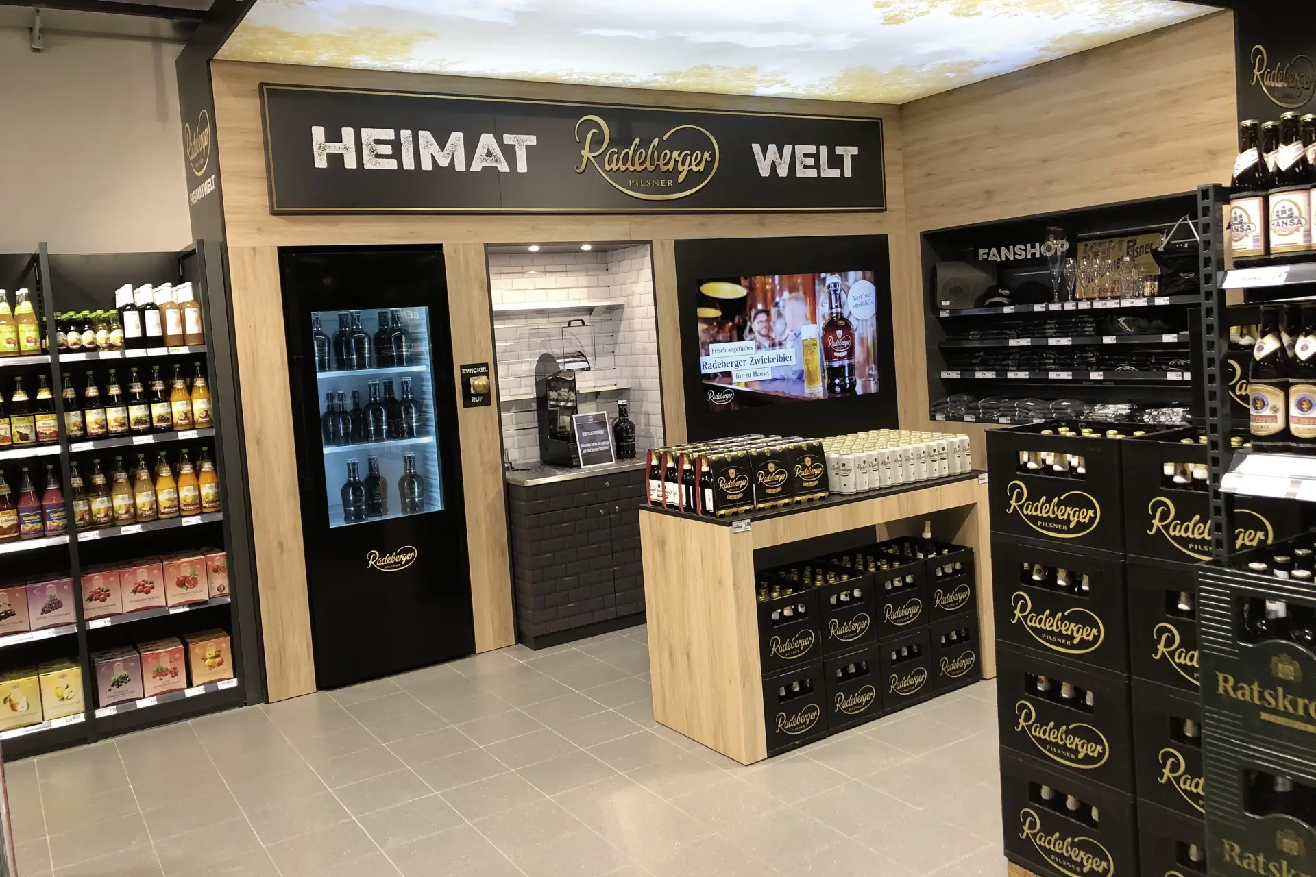 A room with beer crates, bottles, and a refrigerator of the Radeberger brand. A wall with the words Heimat Radeberger Welt.