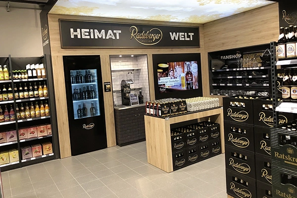 A room with beer crates, bottles, and a refrigerator of the Radeberger brand. A wall with the words Heimat Radeberger Welt.