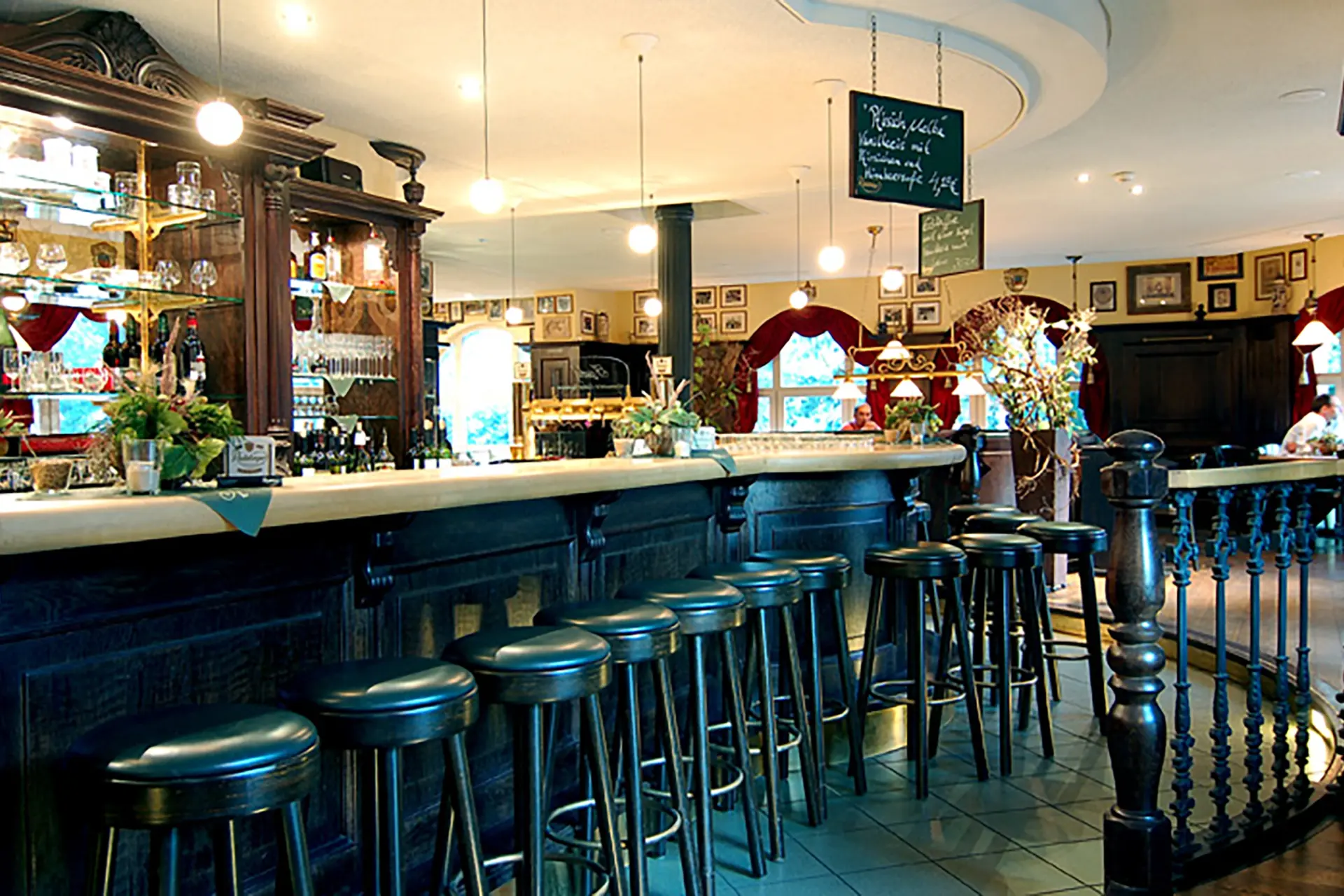 Bar counter with stools and beer taps. Warm lit room with shelves bottles and framed pictures.