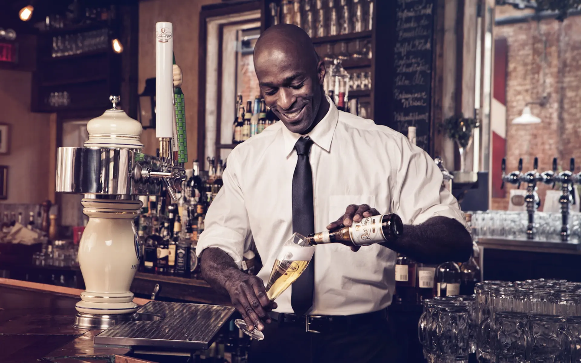 A smiling man pours Radeberger beer into a Radeberger beer glass.
