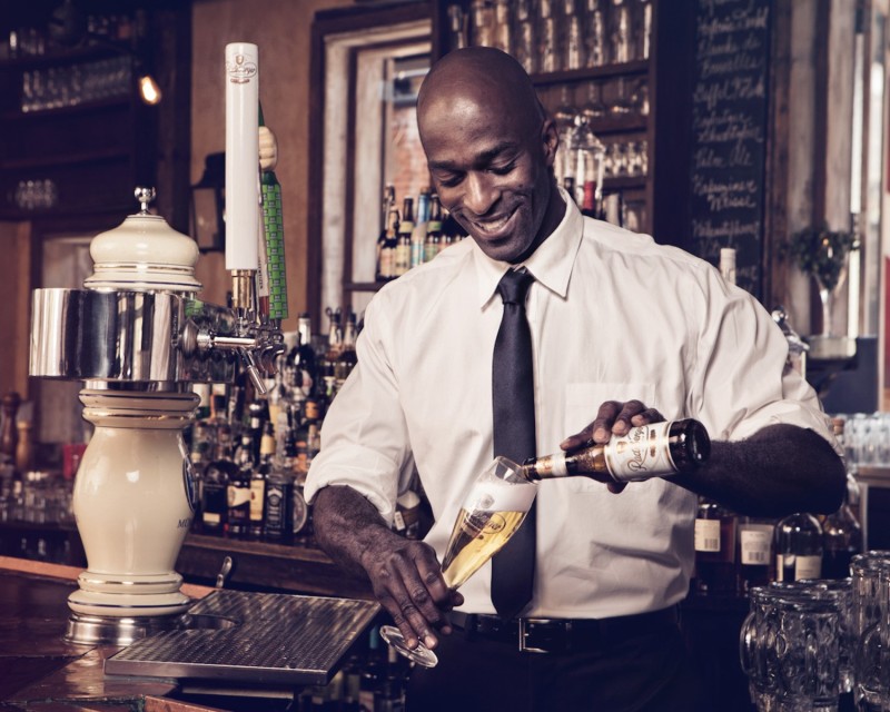 A smiling man pours Radeberger beer into a Radeberger beer glass.